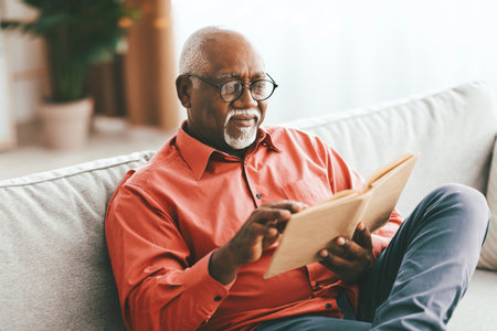 Elderly Man Reading a Book in a Cozy Living Room During the Afternoonの写真素材