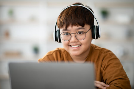 Cheerful Boy Engaged in Online Lesson Using Laptop and Wireless Headsetの写真素材