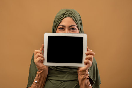Muslim Woman in Hijab Presents Digital Tablet With Blank Screen in Studio Settingの写真素材