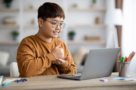 Cheerful Teenager Enjoys Online Lesson and Gives Thumbs up in Cozy Home Settingの写真素材