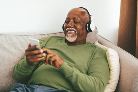 Smiling Senior Man Enjoying Music While Relaxing on the Couch at Home