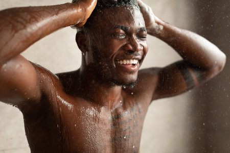Black Male Relaxes Under Warm Water While Washing Hair Indoors in Bathroomの写真素材