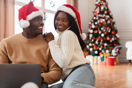 Cheerful Black Couple Enjoying Christmas Eve Shopping Online Together at Homeの写真素材