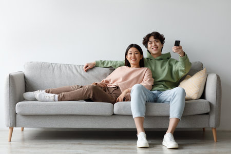 Young Asian Couple Enjoys Movie Night Together on Sofa While Switching Channelsの写真素材