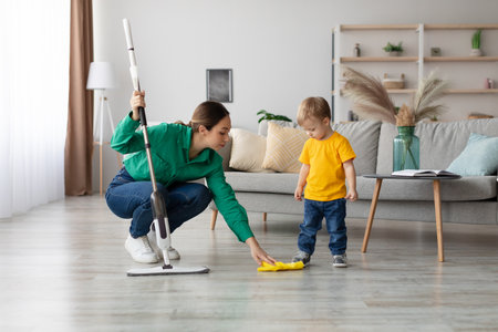 Mother Teaches Child to Help With Cleaning While Using a Steam Mop in a Cozy Living Roomの写真素材