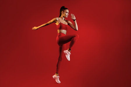 Fitness Model Strikes a Dynamic Pose in Vibrant Red Workout Gear Against a Bold Backgroundの写真素材