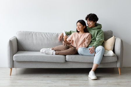 Young Asian Couple Enjoys Social Media Together While Relaxing on Their Couch at Homeの写真素材