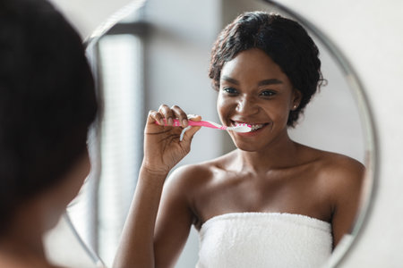 Young Black Woman Enjoys Morning Routine While Brushing Her Teeth in Front of Mirror