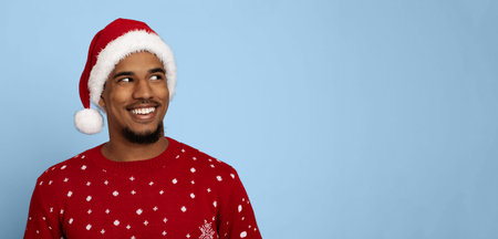 Joyful Man in Christmas Sweater and Hat Smiling Against Blue Background During Holiday Seasonの写真素材