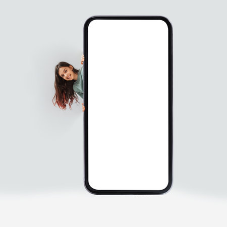 Cheerful Girl Posing With Large Blank Cellphone on Gray Background for Educational App Promotionの写真素材