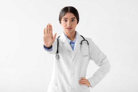 Hindu Female Doctor in Coat Showing Stop Gesture During Medical Work in a Studio Settingの写真素材