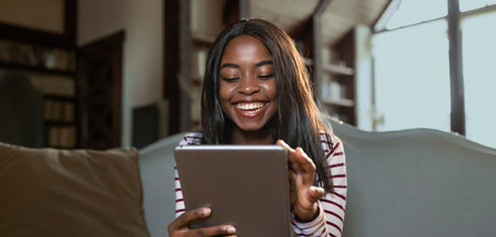 Woman Enjoys Using Tablet While Sitting on Sofa at Home During Daylight Hours