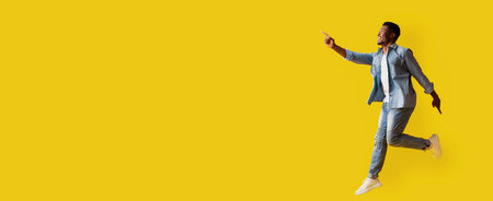 Man in Blue Suit Celebrates With Joy Against a Bright Yellow Background While Pointing Upwards