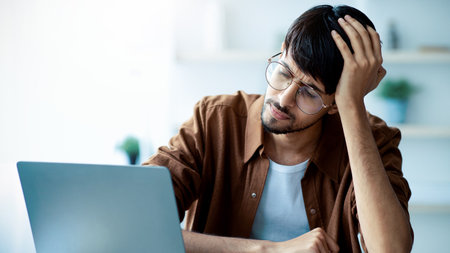 Man Experiencing Frustration While Working on Laptop in Bright Workspace