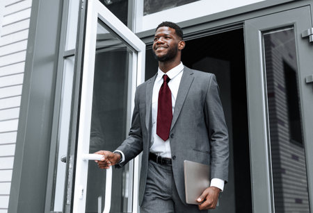 Businessman Steps Outside a Modern Office Building With Confidence and Styleの写真素材