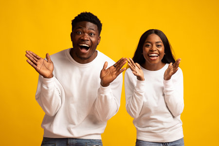 Two Friends Celebrate Joyfully Against a Vibrant Yellow Background in Casual Attireの写真素材