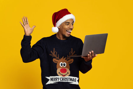 Excited Man in Christmas Sweater Waving at Laptop During Virtual Celebrationの写真素材