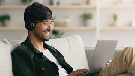Man in Headphones Enjoying Music While Working on Laptop at Home in Cozy Living Room