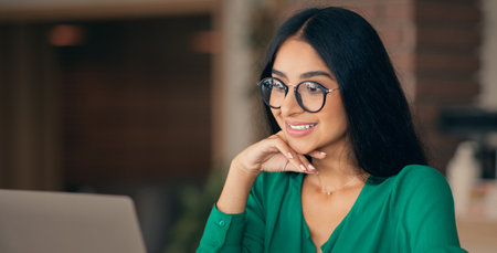 Woman in Green Blouse Smiles While Working on Laptop in a Cozy Indoor Space
