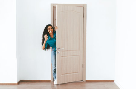 Smiling Woman Peeking Through a Door in a Bright and Airy Roomの写真素材