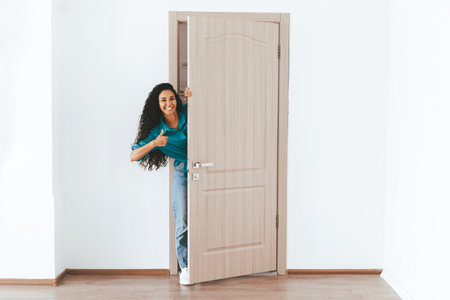 Woman Smiling and Giving Thumbs up While Standing at Open Door in Empty Roomの写真素材
