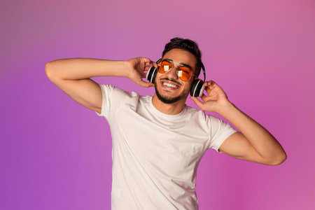 Relaxed Young Arab Man Enjoys Music With Wireless Headphones Under Neon Lightsの写真素材