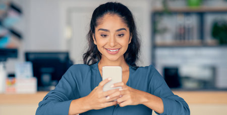 Young Woman Smiles While Using Smartphone in a Bright Indoor Setting During the Dayの写真素材