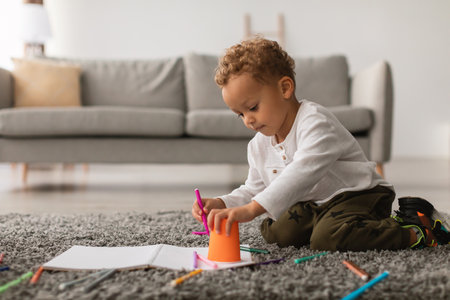 Little Boy Uses Colorful Markers to Draw at Home in Cozy Living Room During Leisure Timeの写真素材