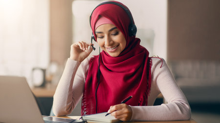 Young Woman Studying Online While Taking Notes in a Notebook With Headphones Onの写真素材