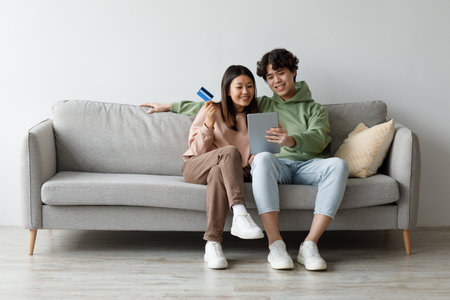 Young Couple Enjoys Online Shopping Together on Their Sofa at Homeの写真素材