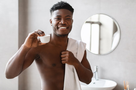 Black Man Showcasing Moisturizer Cream in Bathroom While Smilingの写真素材