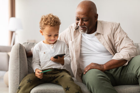 Grandfather and Grandson Enjoy Mobile Games Together in Cozy Home Settingの写真素材