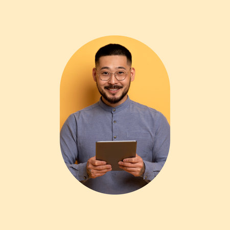 Smiling Man Holding a Tablet and Looking at the Camera Against a Yellow Backgroundの写真素材