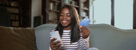 Smiling Young Woman Enjoying Online Shopping at Home With a Smartphone and Credit Card