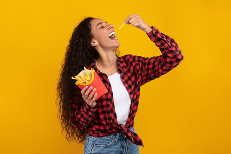 Excited Latin Lady Enjoys Tasty French Fries in Bright Orange Studio Background