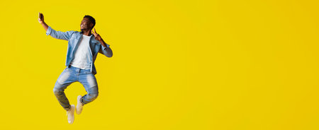 Man Jumping Joyfully While Taking a Selfie on a Bright Yellow Backgroundの写真素材