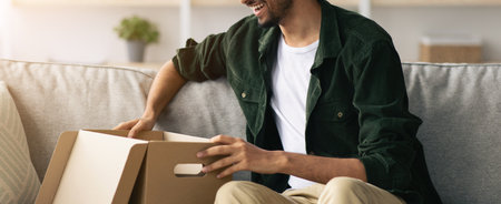 Excited Man Opening a Box While Sitting on a Sofa in a Cozy Living Roomの写真素材