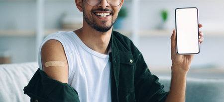 Young Man Showing Vaccination Record on Smartphone With a Bandage on His Arm in a Cozy Settingの写真素材