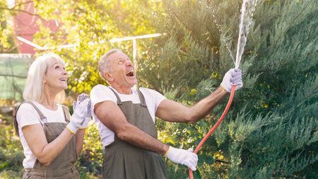 Elderly Couple Enjoys Watering Garden Plants on a Sunny Day in Their Backyardの写真素材