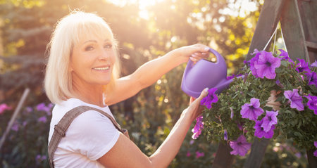 Gardening Joy in a Sunny Garden With Vibrant Flowers and a Smiling Woman Watering Plantsの写真素材
