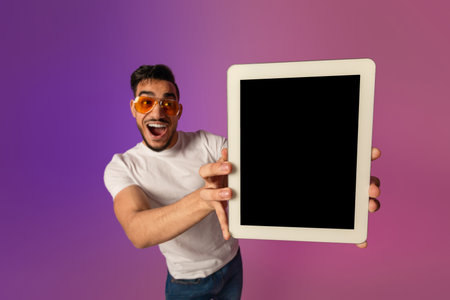 Excited Arab Man Shows Blank Tablet Screen in Neon Lights for App Mockup Displayの写真素材
