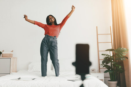 Joyful Woman Dancing on Bed in Bright Bedroom During Sunny Dayの写真素材