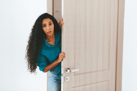 Woman Curiously Peeking Through a Partially Open Door in a Bright Roomの写真素材