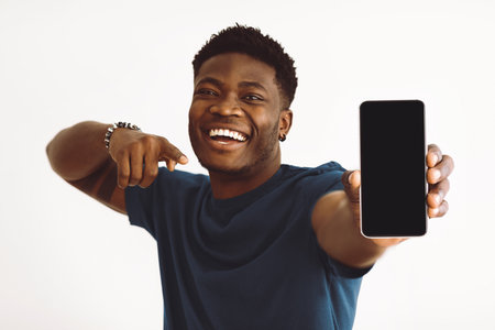 Young Man Smiles and Showcases Smartphone With Excitement Indoorsの写真素材
