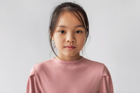 Serious Asian Girl in Pastel Pink Top Poses for Portrait Against Gray Background in Studioの写真素材