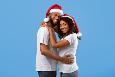 African american lovers in Santa hats embracing on yellow studio background, celebrating New Year 2022 or Christmasの写真素材