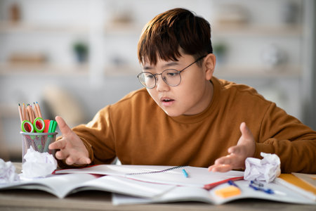 Korean Teenager Struggles With Homework at a Table in a Cozy Home Environmentの写真素材
