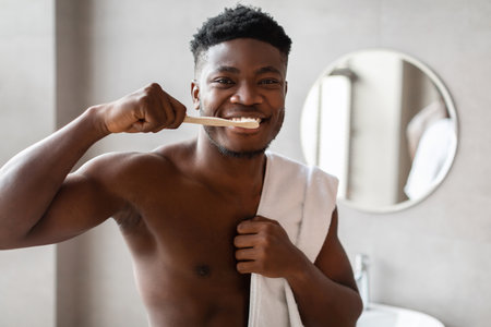 African American Man Smiling While Brushing Teeth in Modern Bathroom at Homeの写真素材