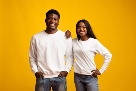 Smiling Young Man and Woman Posing Together in White Outfits Against a Bright Yellow Backgroundの写真素材