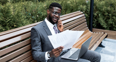 Businessman in Suit Reviews Documents While on Phone in Outdoor Settingの写真素材